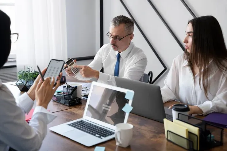 Colleagues working at a shared desk with laptops, phones and a calculator