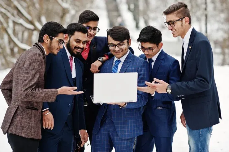 Group of young men in suits looking at a laptop outdoors in snow
