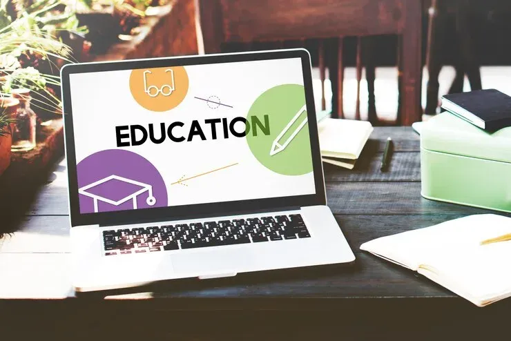 Laptop on a wooden desk showing the word Education with simple icons