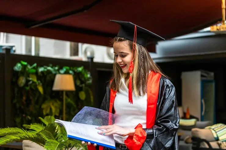 Smiling graduate in cap and gown reading a book