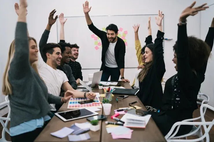 Team celebrating with raised hands around a meeting table