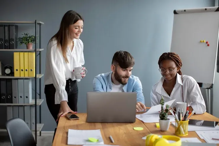 Three colleagues reviewing documents together at a laptop in an office