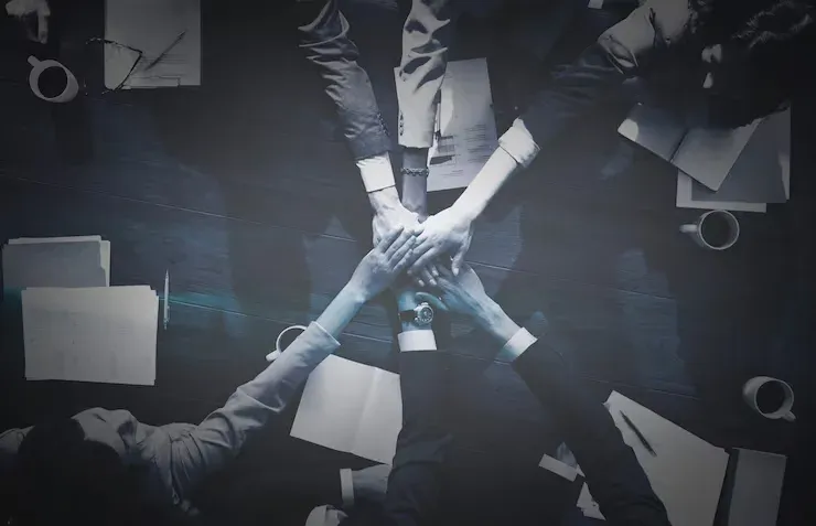 Team stacking hands over a desk covered in papers, seen from above