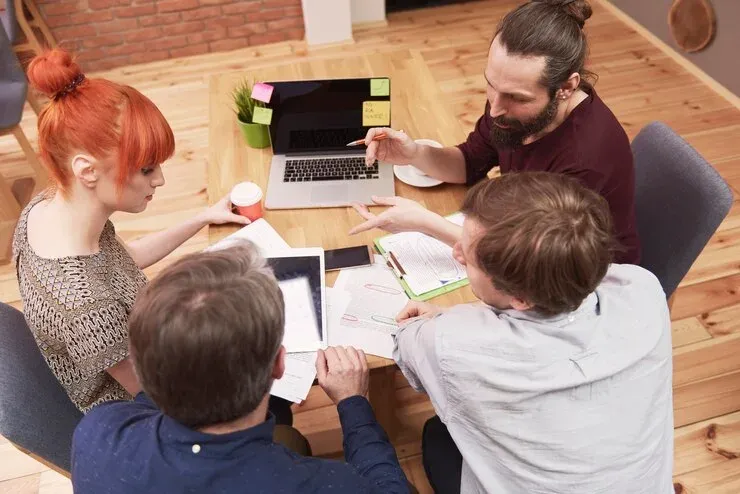 Four colleagues collaborating around a table with a laptop, tablet and papers