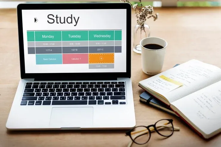 Laptop displaying a weekly study timetable on a desk with coffee and a notebook