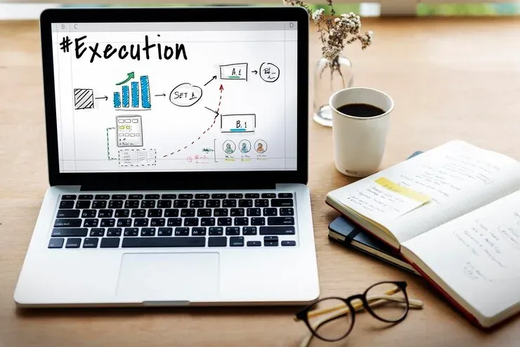 Laptop showing an execution plan sketch on a desk with coffee and a notebook