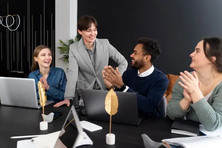 Colleagues smiling and applauding around a table with laptops