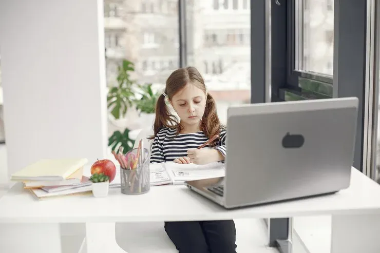 Young girl writing at a desk beside a laptop
