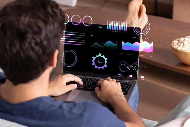 Man using a laptop showing colourful data charts and dashboards